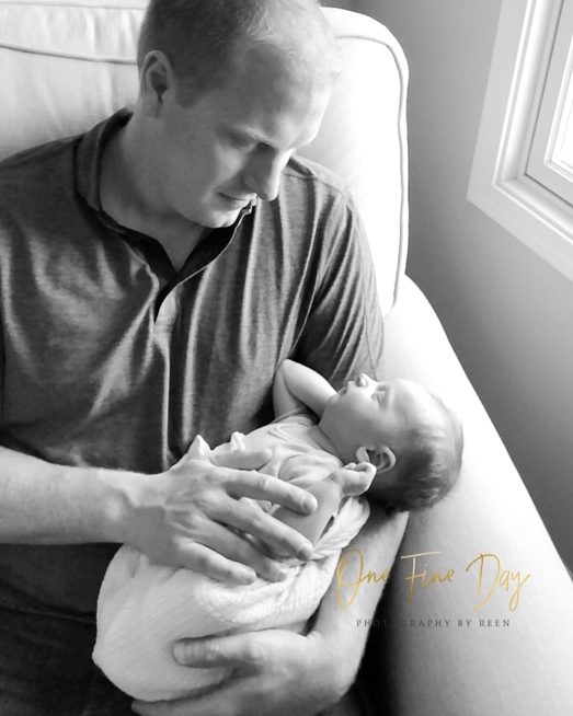 black and white photo by one fine day photography by reen of dad holding newborn baby in rocking chair