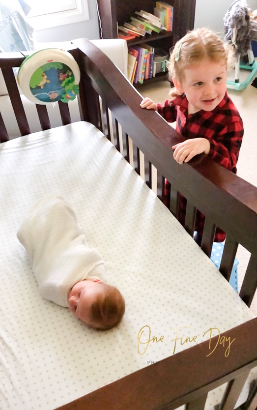 toddler brother peers over crib to look at newborn baby